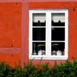 Hvidt sprossevindue i en rød bindingsværksfacade med synlige rammer og glas.