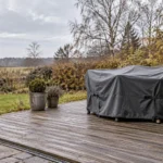 Illustrativ terrasse i en dansk have med ren træbelægning, fri afvanding og havemøbler dækket til for vinteren.