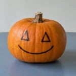 Helt orange græskar med to trekantede øjne og en smilende mund tegnet på skallen.