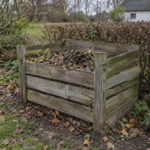 En slidt kompostbeholder af træ med blade og planterester i en efterårshave
