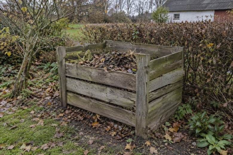 En slidt kompostbeholder af træ med blade og planterester i en efterårshave